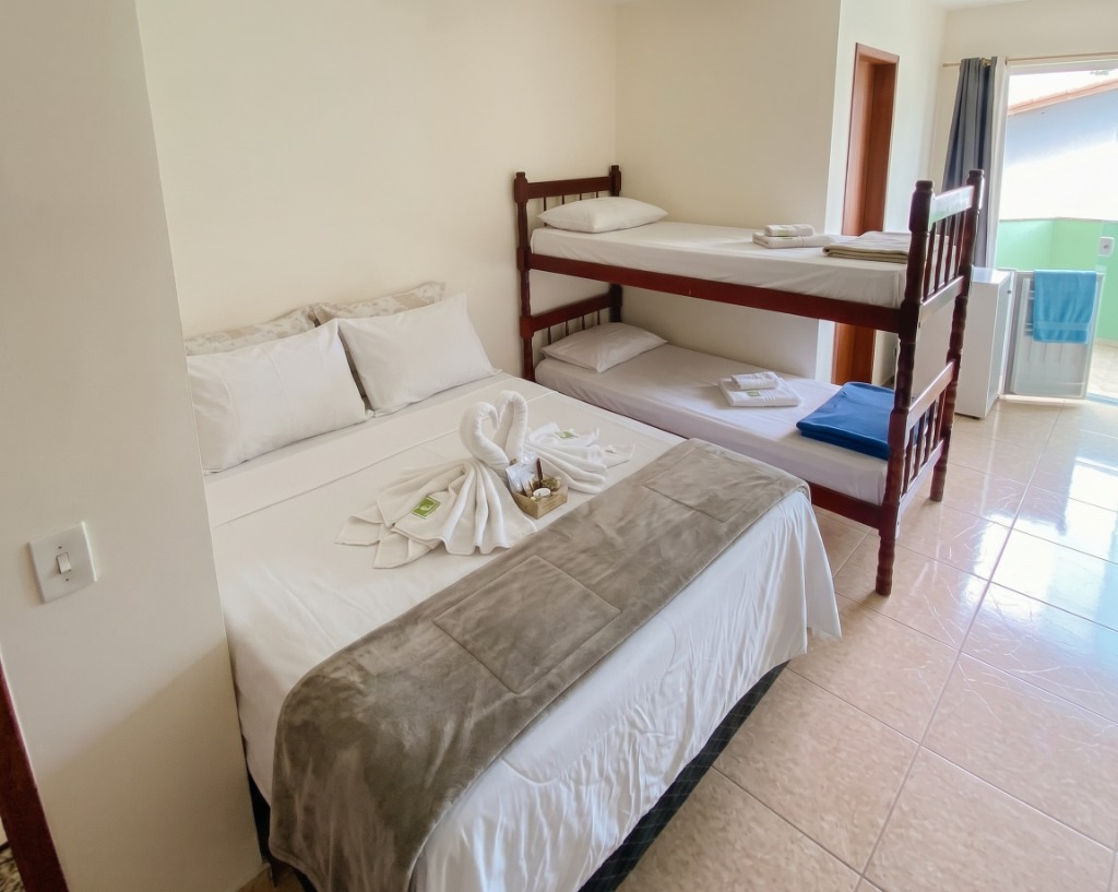 Quarto triplo com cama de casal, cisnes de toalha e um beliche ao fundo